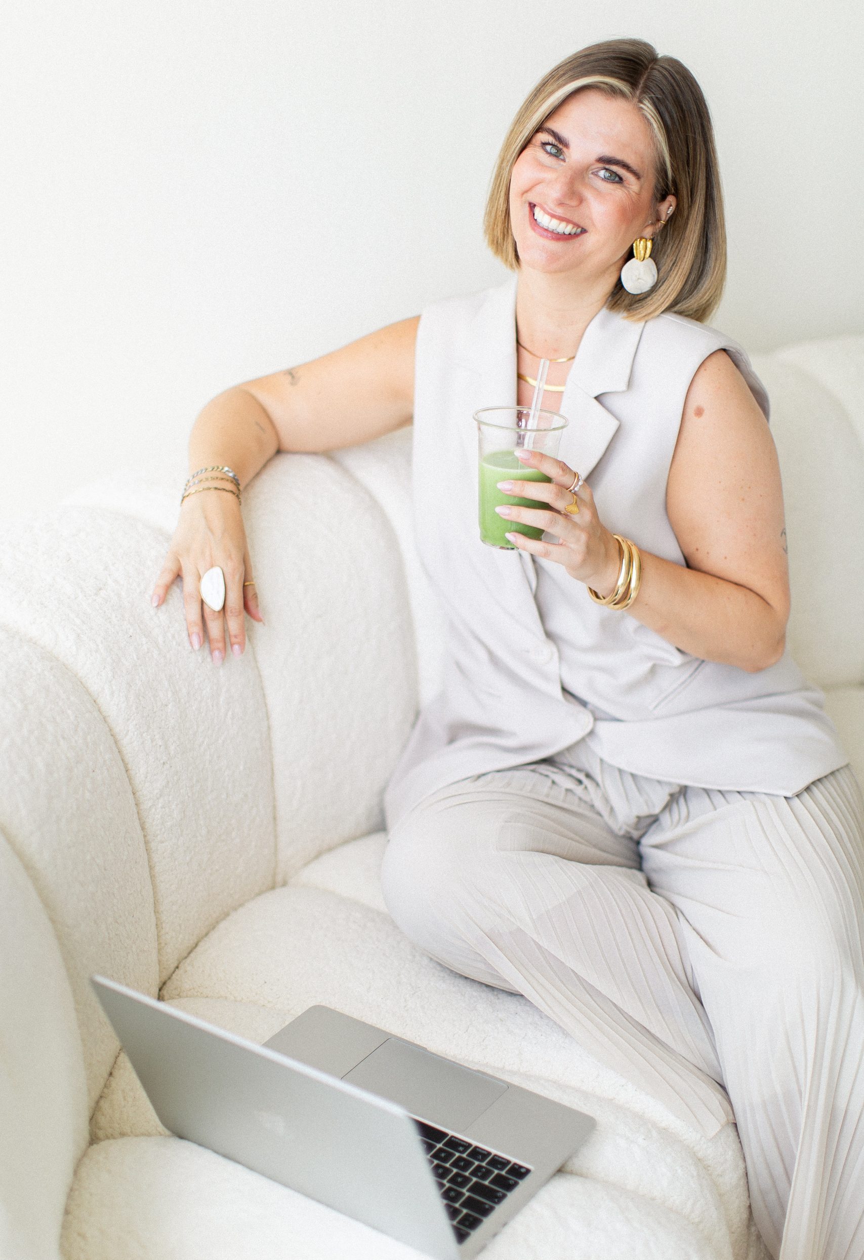 Sabrina sitzt mit einem Matcha in der Hand und ihrem laptop auf einer beigen Couch
